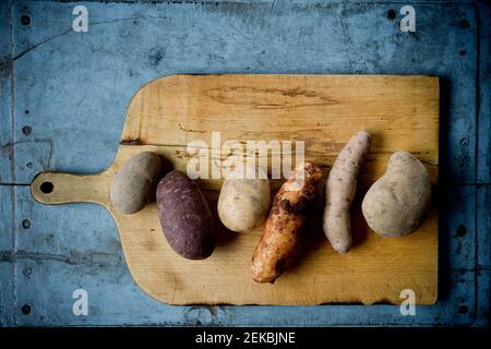 Différentes variétés de pommes de terre sur une planche à découper rustique Banque D'Images