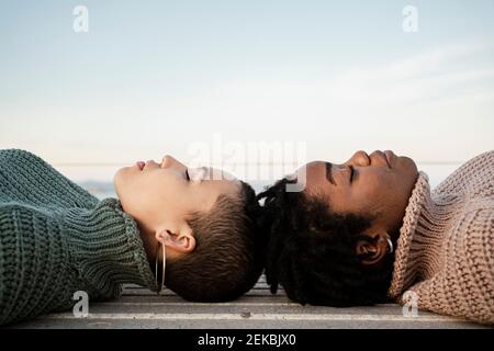 Amis femelles avec les yeux fermés, allongé sur le banc contre le ciel Banque D'Images