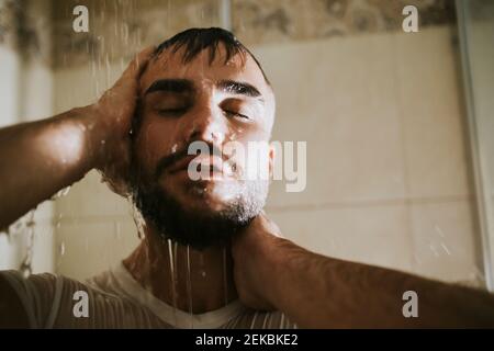 Homme barbu avec les yeux fermés prenant la douche dans la salle de bains Banque D'Images