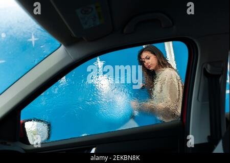 Jeune femme pulvérisant de l'eau sur la fenêtre au lavage de voiture Banque D'Images