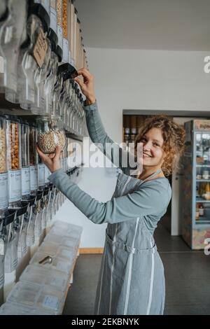 Une femme souriante qui utilise un distributeur de produits alimentaires tout en travaillant aucun magasin de déchets Banque D'Images
