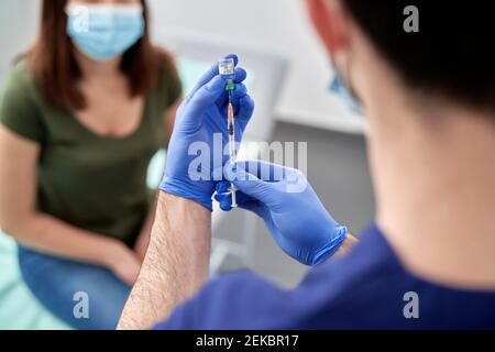 Un médecin de sexe masculin prépare une seringue avec la vaccination COVID-19 pour une patiente Banque D'Images