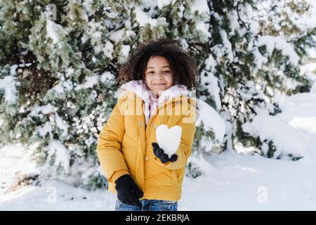 Jolie fille souriante tenant la neige en forme de coeur dans le parc Banque D'Images