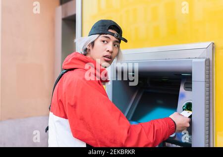 Un jeune homme retire de l'argent à un distributeur automatique de billets Banque D'Images