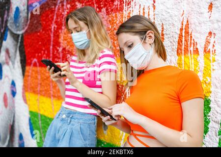 Des amies qui utilisent un téléphone portable tout en se penchant sur un mur peint Banque D'Images