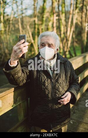 Femme âgée qui prend le selfie par téléphone portable tout en étant debout Passerelle pendant COVID-19 Banque D'Images