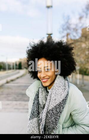 Femme afro souriante avec les mains dans les poches debout à l'extérieur pendant hiver Banque D'Images