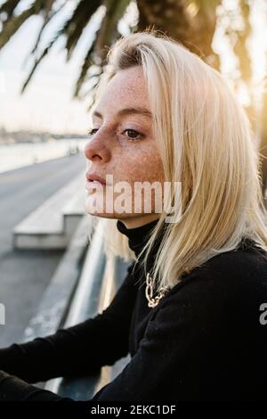 Jeune femme avec des taches de rousseur penchées sur la main contre le palmier Banque D'Images