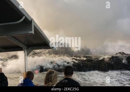 Les visiteurs sur un bateau regardent la rivière de lave qui coule dans l'océan Pacifique depuis le volcan Kilauea. Banque D'Images