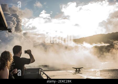 Les visiteurs sur un bateau regardent la rivière de lave qui coule dans l'océan Pacifique depuis le volcan Kilauea. Banque D'Images