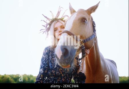 Femme portant des fleurs tenant le cheval contre le ciel clair Banque D'Images