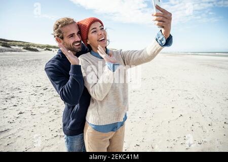 Portrait d'un jeune couple debout ensemble sur la plage et en utilisant smartphone Banque D'Images