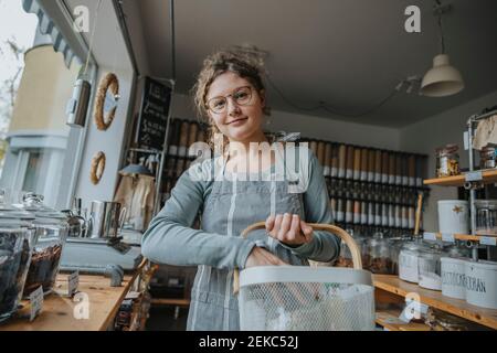 Une femme souriante tient le panier tout en travaillant sans gaspillage boutique Banque D'Images