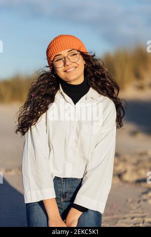 Femme souriante dans des lunettes contre le ciel en regardant loin à la plage Banque D'Images
