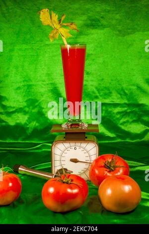 Verre de jus sur balance par tomates fraîches contre tissu vert Banque D'Images