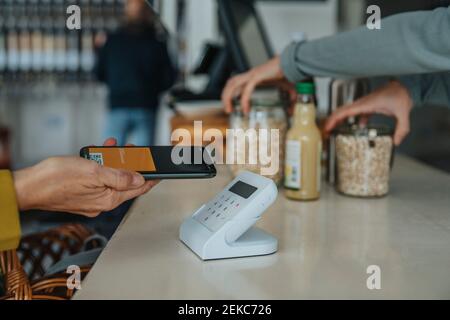 Client mature avec téléphone mobile payant par lecteur de code-barres en magasin Banque D'Images