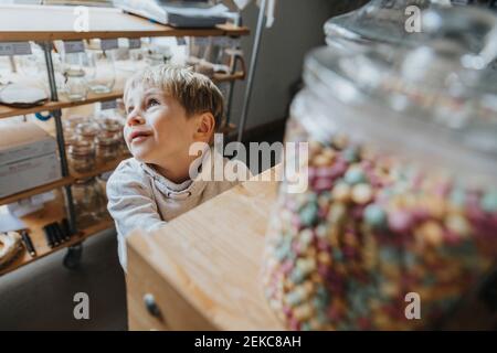 Un petit garçon blond rêve en se tenant dans un magasin de bonbons Banque D'Images