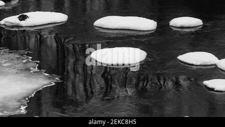 La rivière au printemps avec des formations de neige rondes sur le rochers dans l'eau sombre Banque D'Images