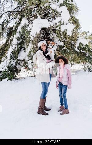 Famille heureuse avec un chien debout dans la neige au parc pendant hiver Banque D'Images