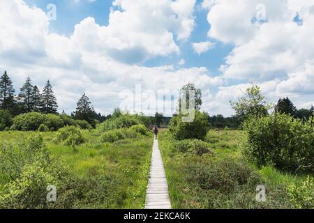 Homme marchant sur la promenade dans le parc naturel de High Fens contre ciel nuageux Banque D'Images