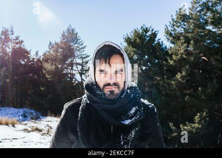 Homme barbu dans des vêtements chauds debout sur une terre enneigée contre le ciel Banque D'Images