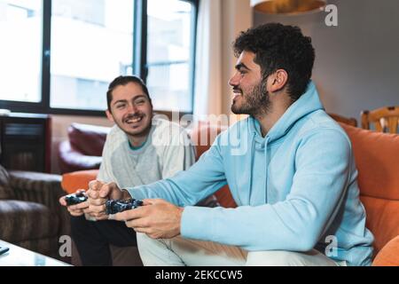 Des jeunes amis souriants discutent tout en jouant à un jeu vidéo à la maison Banque D'Images