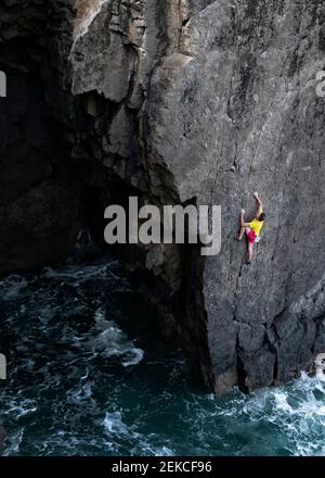 Alpiniste mâle déterminé grimpant sur la falaise par la mer Banque D'Images