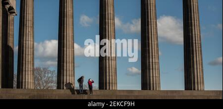 Couple solitaire sur les marches du monument national écossais sur Calton Hill, Édimbourg lors d'une journée ensoleillée pendant l'enfermement 2021 Banque D'Images