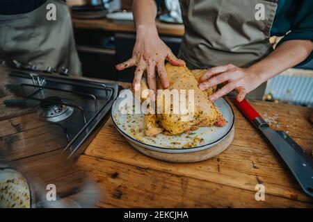 Chef mariner de la viande de poulet tout en étant debout par un collègue dans la cuisine Banque D'Images