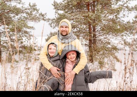 Le père embrasse son fils et sa fille tout en se tenant contre les arbres à l'intérieur forêt en hiver Banque D'Images