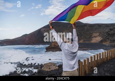 Un jeune touriste agite le drapeau arc-en-ciel tout en se tenant au point de vue El golfo, Lanzarote, Espagne Banque D'Images