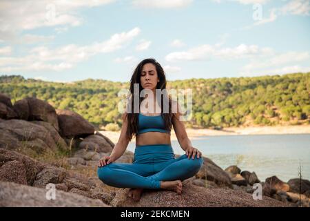 Jeune femme méditant tout en étant assise à pattes croisées sur le rocher Banque D'Images