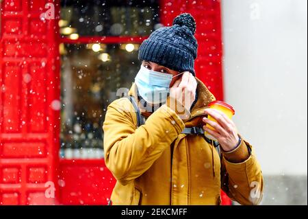 Homme en vêtements chauds portant un masque de protection tout en se tenant contre le magasin pendant COVID-19 Banque D'Images
