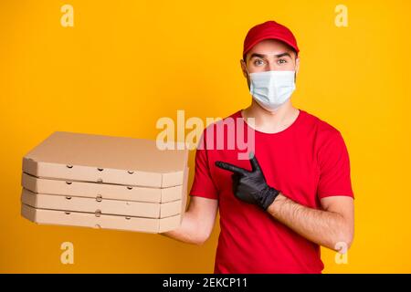 Portrait de gentil mec porter un masque apportant des boîtes à pizza de démonstration les soins de santé se isolent sur fond jaune vif Banque D'Images