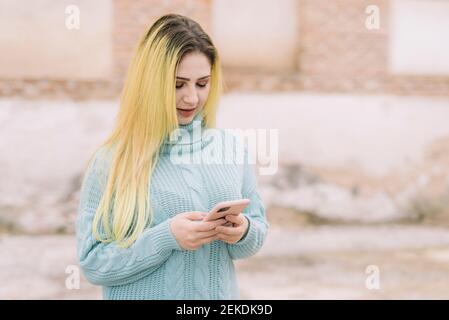 Modèle de femme blond foncé portant un pantalon noir et bleu sweater dans la rue à l'aide d'un smartphone avec espace de copie Banque D'Images