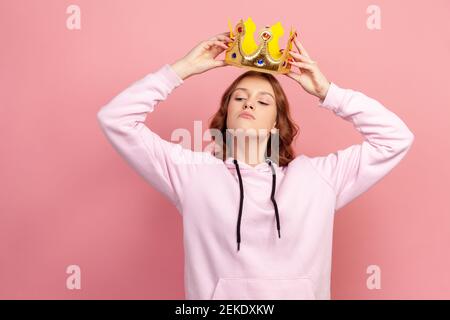 Portrait d'une jeune fille adolescente à poil dur égoïste tenant la couronne d'or sur la tête, regardant avec arrogance, statut privilégié. Prise de vue en studio en intérieur Banque D'Images