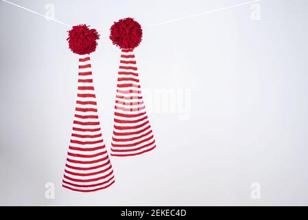 Deux casquettes rayées rouges et blanches avec une longue queue et une grande pompons rouges sont suspendues sur une corde blanche sur un fond blanc. Banque D'Images