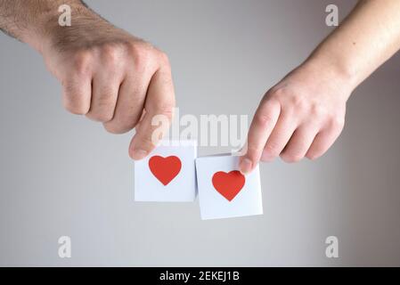Une main femelle et une main mâle tenant deux boîtes blanches avec des coeurs rouges sur un fond blanc, gros plan Banque D'Images