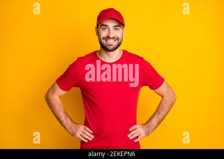 Photo de joyeux homme de livraison confiant porter une tenue rouge sourire mains bras taille isolé couleur jaune arrière-plan Banque D'Images