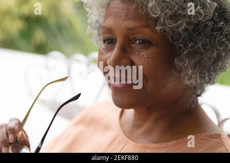 Portrait d'une femme afro-américaine âgée tenant des lunettes souriant assis sur le porche Banque D'Images