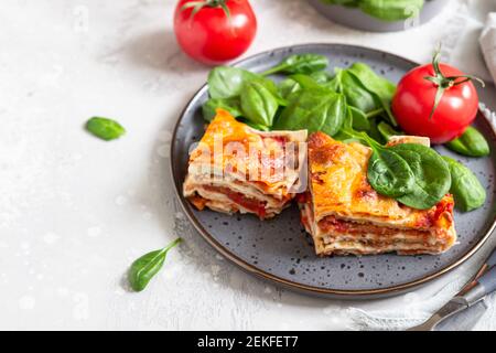 Lasagnes italiennes à la sauce tomate et au fromage, servies avec des tomates et des épinards, sur fond de béton léger. Lasagnes végétariennes faites maison. Mise au point sélective Banque D'Images