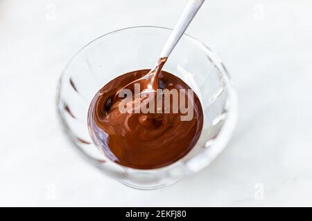 Gros plan de la cuillère mélangeant le liquide remuant le chocolat chaud fondu crème glacée sauce au sirop dans un petit bol en verre Banque D'Images