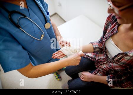 Vue rapprochée du dessus de l'infirmière tout en aidant la patiente avec un bandage médical dans le bureau de l'hôpital. Banque D'Images