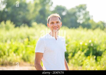 Bokeh vert doux pré fond dans le parc naturel avec portrait de sourire jeune heureux homme en été en chemise blanche Banque D'Images
