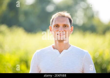 Arrière-plan vert bokeh doux dans un parc naturel avec portrait de gros plan de sourire jeune heureux homme en été en chemise blanche Banque D'Images