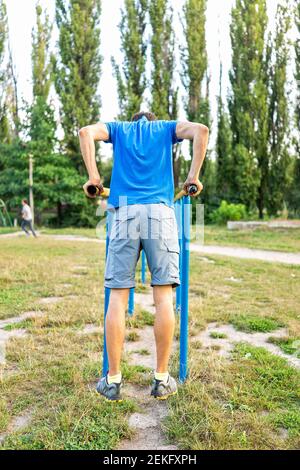 FIT jeune homme faisant de la calisthénique exercice d'équilibrage sur des barres horizontales parallèles exercice dans le parc extérieur à Rivne, Ukraine aire de jeux vue verticale Banque D'Images
