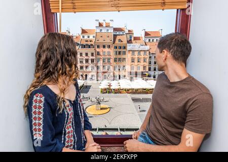 Les jeunes hommes et femmes aiment couple assis sur le bord de la fenêtre de l'appartement regardant la vue de l'ancienne place du marché dans la ville historique de Varsovie, Pologne Banque D'Images