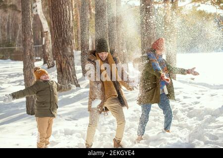 Joyeux jeune homme, sa femme et sa petite fille en hiver chaud jouant des boules de neige tout en s'amusant dans la forêt d'hiver parmi les arbres Banque D'Images