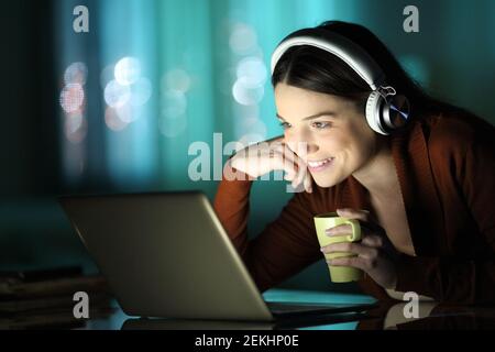 Bonne dame regardant des vidéos sur un ordinateur portable assis dans la nuit à la maison Banque D'Images
