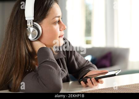 Femme pensive portant un casque sans fil qui envisage d'écouter de la musique à accueil